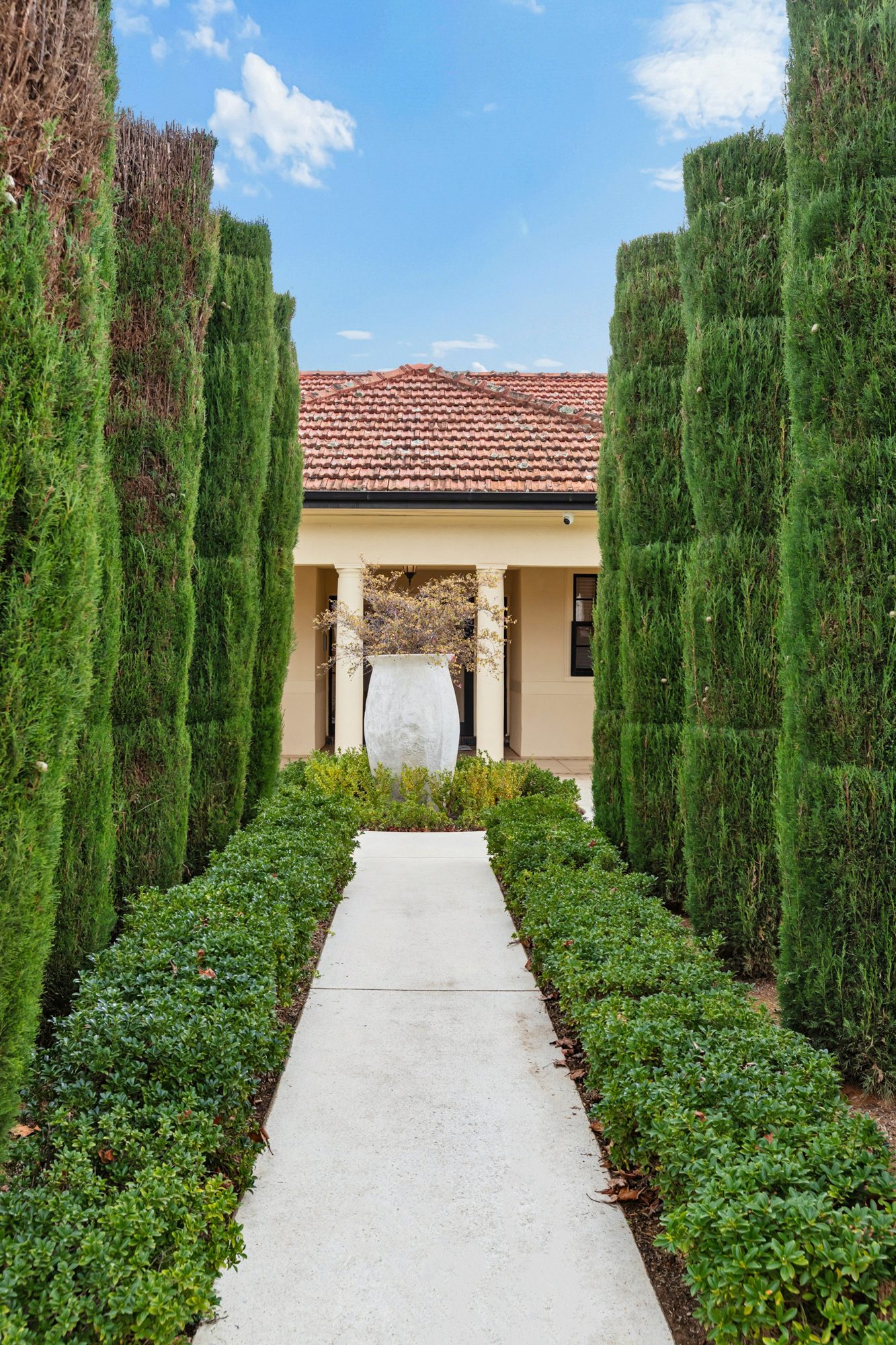 A straight garden path framed by tall clipped hedges leads to the front porch